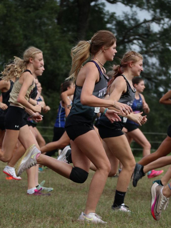 JUST GETTING STARTED. As the varsity girls race begins, sophomore Kinley Gibbs starts with her teammates. Gibbs was unable to finish the race because of a knee injury and being overheated.
