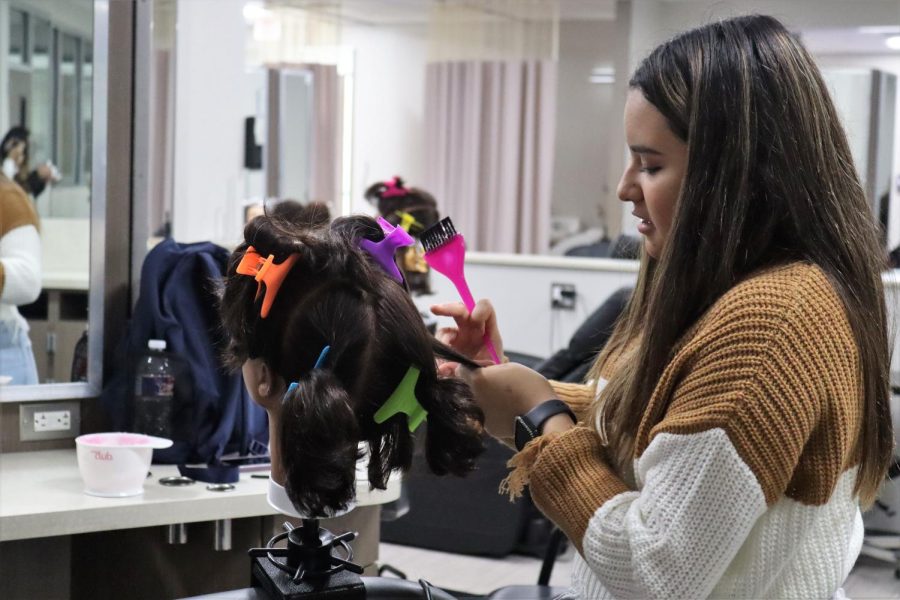 PIECE BY PIECE. Sectioning off hair, junior Kaci Garcia works on coloring hair with a mannequin. Students practice and perfect their technique before using live models.  