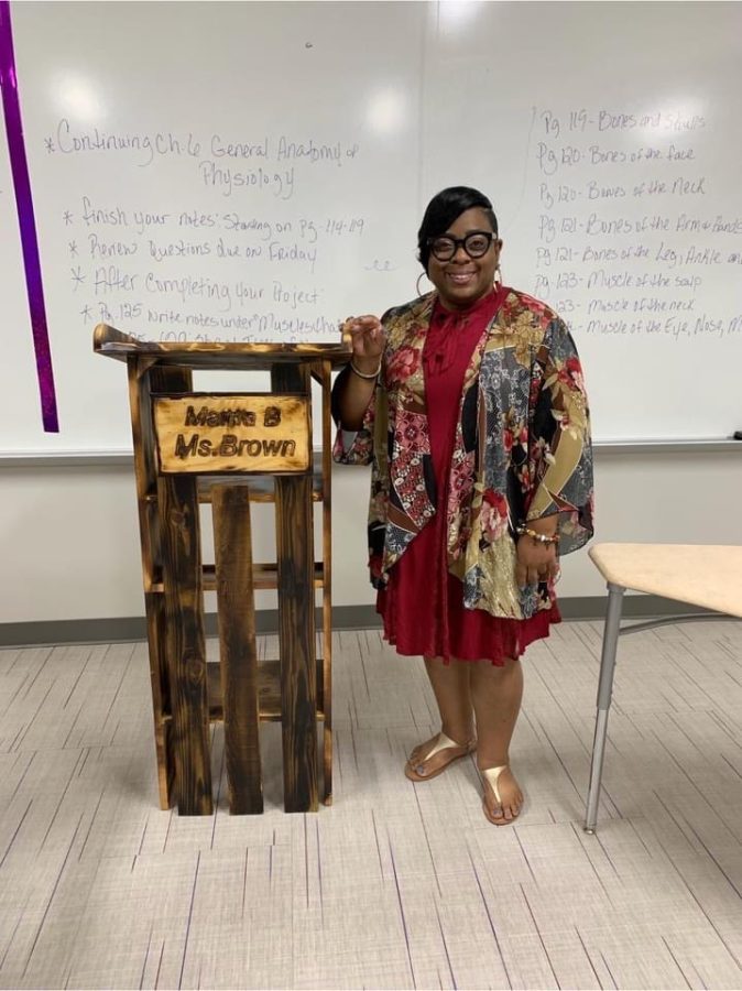 NEVER FORGOTTEN. Proud of her new podium, cosmetology teacher Callie Brown poses with the furniture bearing her name. Brown who fought a valiant fight against cancer, passed away in March.