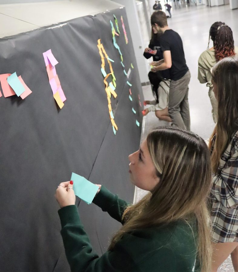 SMALL GESTURES. BIG REWARDS. junior Addison Lyons, a members of the DASH committee of Student Council places post-it notes on a collage across from the cafeteria on the second floor. The group hopes to spread kindness and mental health awareness. 
