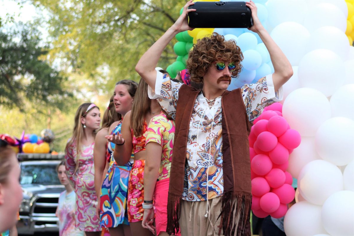 GROOVY WILDKAT. With the swim and dive float, sophomore Aaron Barker shares his 70s vibe and tunes with the parade. photo by Marina Wilson