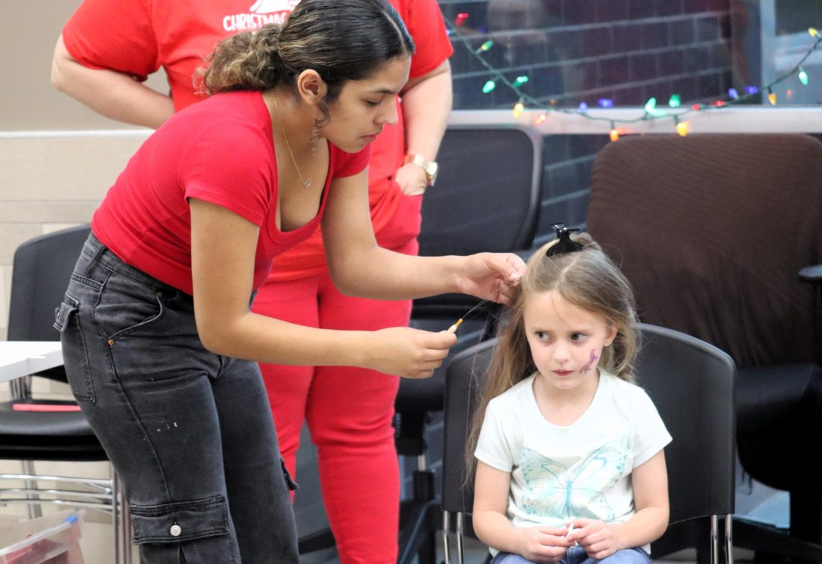 TINSEL TIME.  Working with the cosmetology groups adding tinsel to hair, senior Juliana Hernandez adds a little Christmas spirit to a child.
