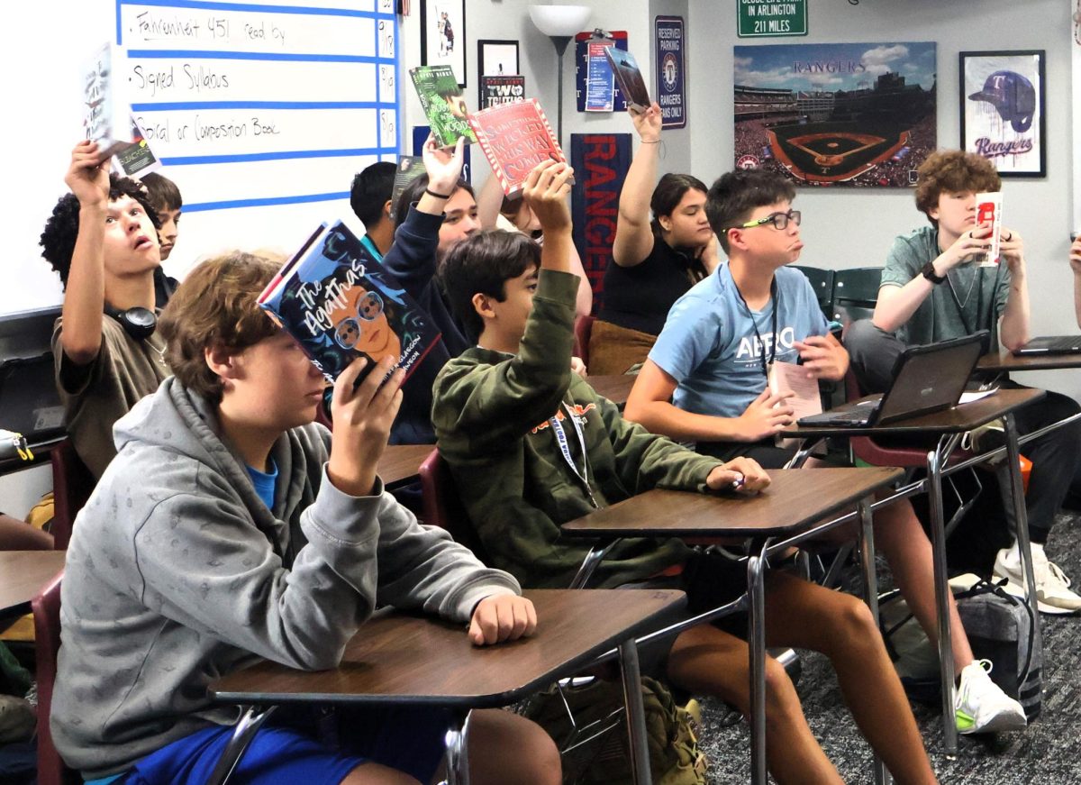 BY THE BOOK. In Chris Slovak's English I honors, students hold up their books during the book speed dating activity in class. Each student picks a book they want to read during their independent reading in class. photo by Heavin Bell