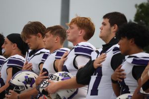 GOD BLESS THE USA. With his hand over his heart, senior Justin Willis joins the team during the national anthem before the game. Thursday games make Fridays tough for players after arriving home late after the game. 