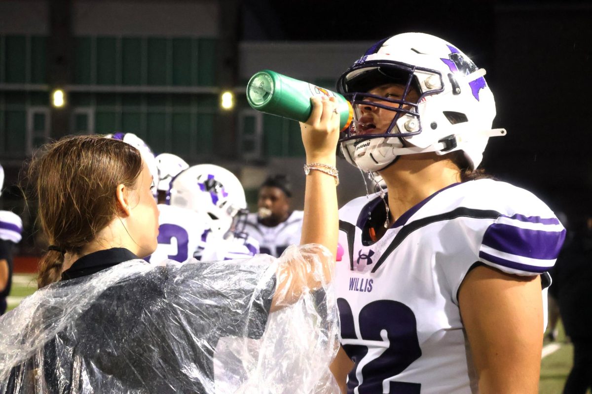 RAIN, RAIN GO AWAY. Wearing her poncho to keep her dry, sophomore Hailey Turner gives sophomore AJ Tuner a drink during a break in the game.  Traveling with the team is part of the trainers' jobs, evern on Thursday games. 