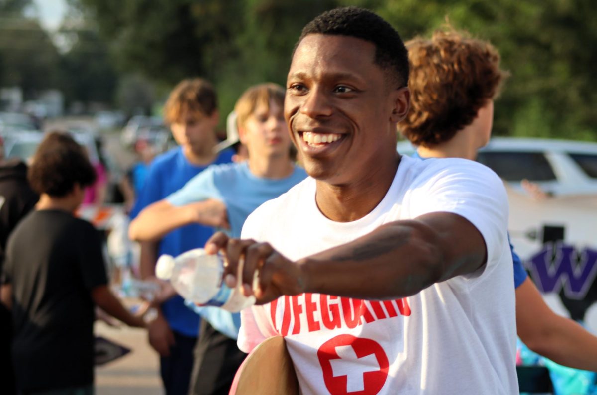 LIFEGUARD ON DUTY. Passing out water to the hot crowd coach John Lewis walks with the swim team.