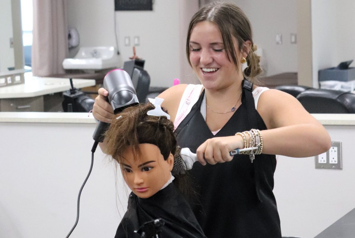 BOOK NOW.  Working on her skills, senior Mallori Mitchell practices her blow drying skills in class. The Wildkat Salon will host a fall salon day on Oct. 26. Haircuts, conditioning treatments, manicures and hard treatments are available. 