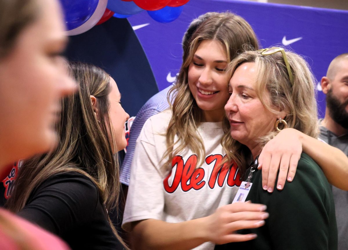 HOTTY TODDY. Sharing a hug with Superintendent Dr. Kimberly James as head coach Kayla Jenkins looks on, senior Carly Paugh celebrates her signing day with a ceremony in the gym. Paugh signed with SEC powerhouse Ole Miss.  photo by Ella McDonald