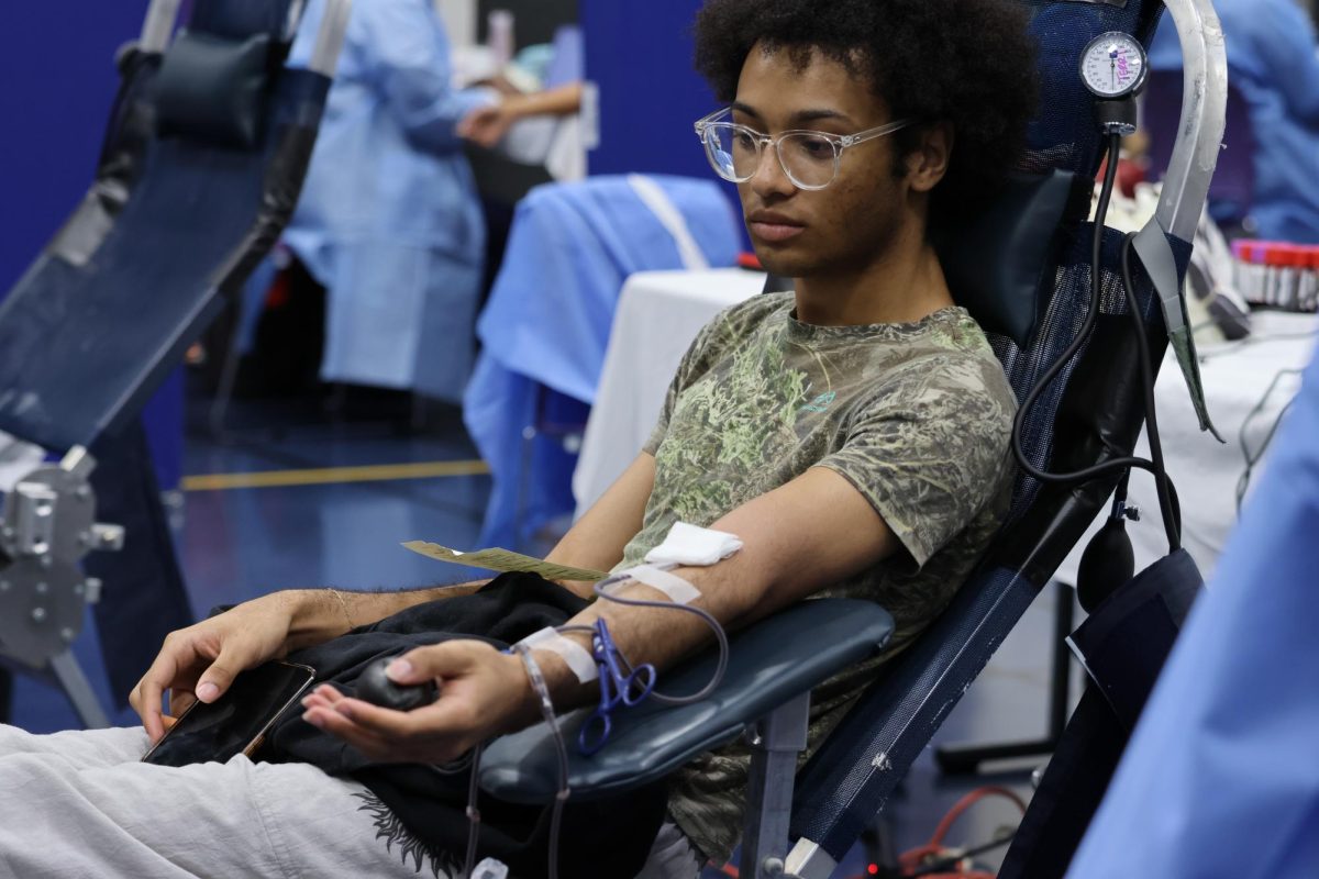 PICTURE THIS. Looking at the people donating blood, junior Isaiah Higgins stays still as junior Brianna Barnett captures his donation.