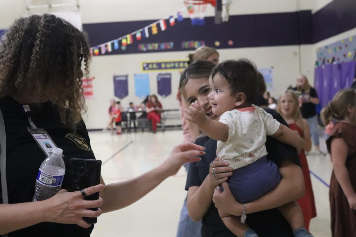 UNEXPECTED SURPRISES. Met with a family friend, senior Natalia Herrera carries baby Issac while Spanish National Honors Society’s sponsor Thesia Sayers plays with him. Bringing together the community to appreciate hispanic culture is the goal of Fiesta Night at C.C. Hardy.