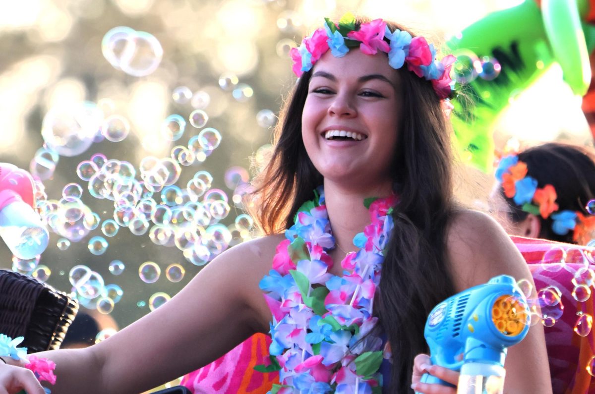 ALOHA. As a member of the swim team junior Claire Mayronne rides in the parade on Wednesday. The float embraced the travel theme of homecoming, Passport to Wildkat Nation. photo by Ashtyn King