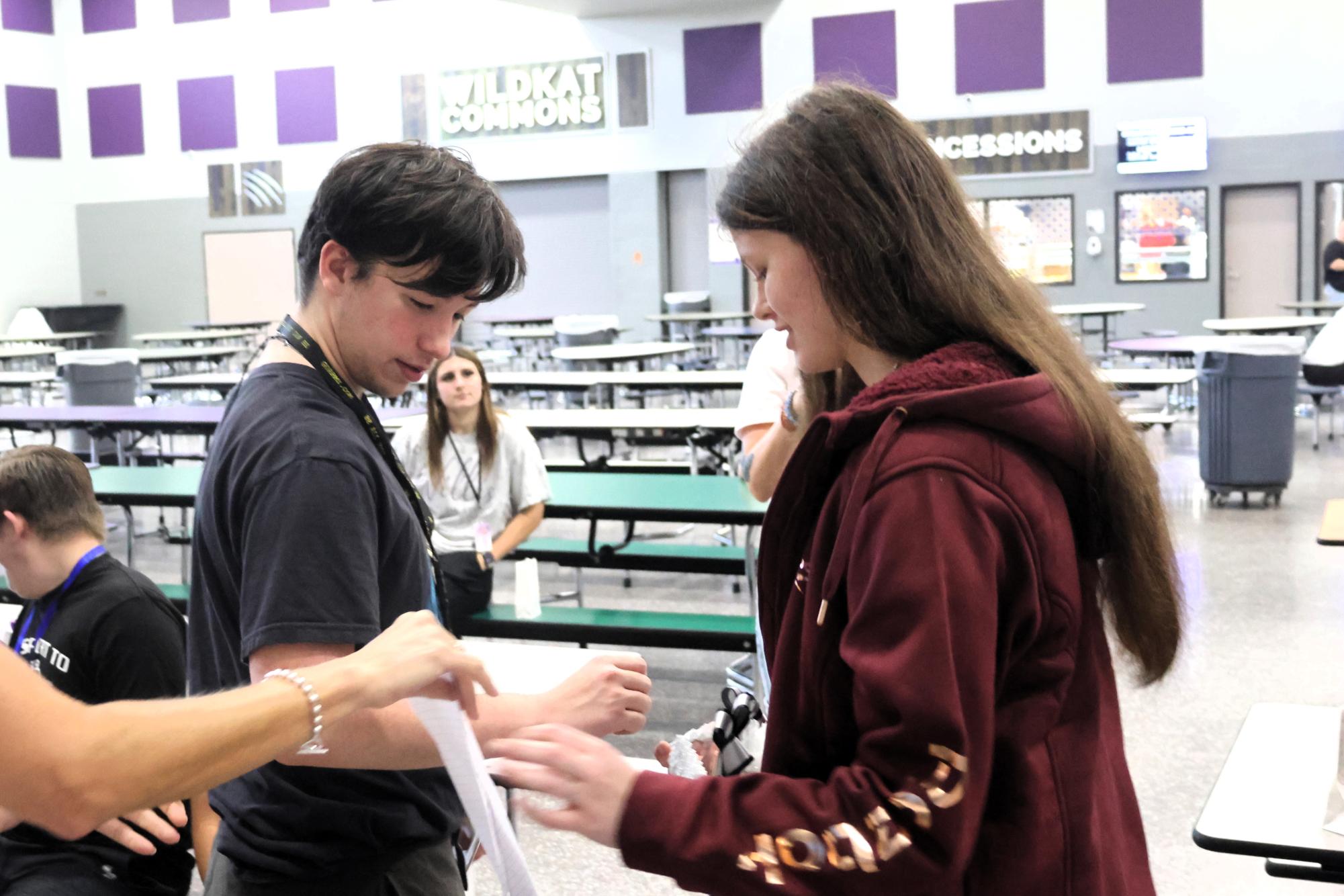 SOMETHING PURPLE. Getting ready to wear hi garter all day, junior Bogart Menie allows junior Kelsi Adams to put the garter around his arm. The members of the floral design class took orders for the mums and garters and created personalized products for students in STRIDE.