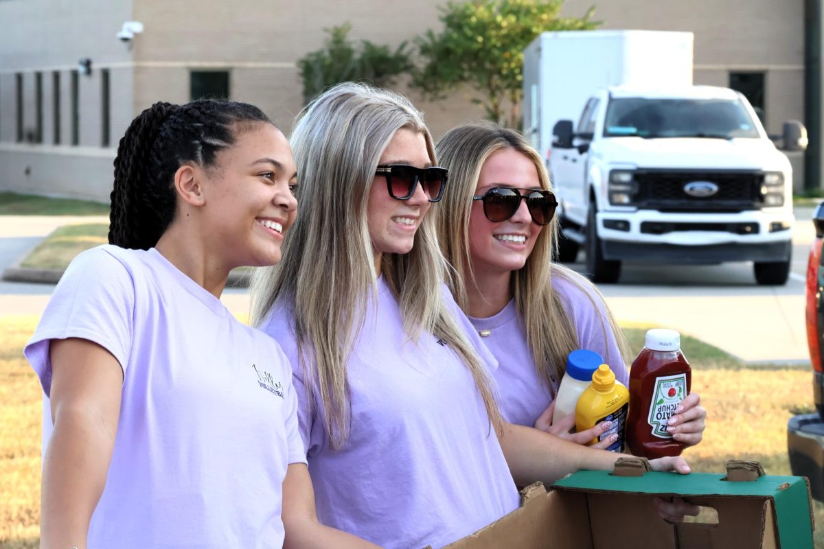 ALL ARE WELCOME. At Fields of Faith, seniors Rylee Foerster, Tori Greeney and Avery Wood welcome visitors to the volleyball booth. The team served food grilled by team parents during the first part of the event. 