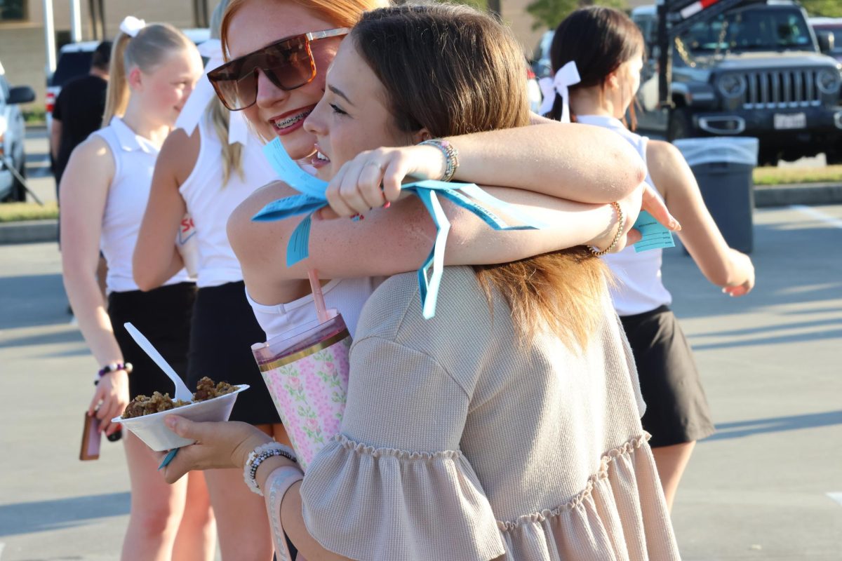 MAKING MEMORIES, Saying hello with a hug, junior Emma Stadler and senior Andreny Hensley embrace in the parking lot as Fields of Faith begins.