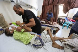 Injured Palestinian Hassan Qlob, 18, who his father says was shot in the head more than two months ago while out seeking food, lies on a bed as he waits for the Rafah crossing to reopen so he can receive treatment abroad, as his father Ibrahim tends to him, after a ceasefire between Israel and Hamas in Gaza went into effect, at Nasser Hospital in Khan Younis, southern Gaza Strip October 15, 2025. REUTERS/Ramadan Abed