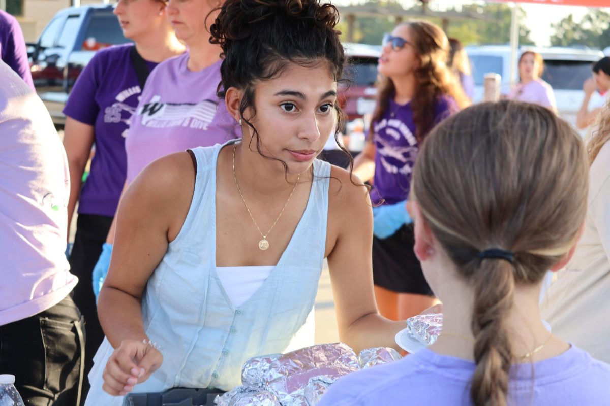 HELPING HANDS. With the tennis team, junior Dayra Rodriguez passes out hotdogs. Sports teams and school clubs joined  FCA in the event. 