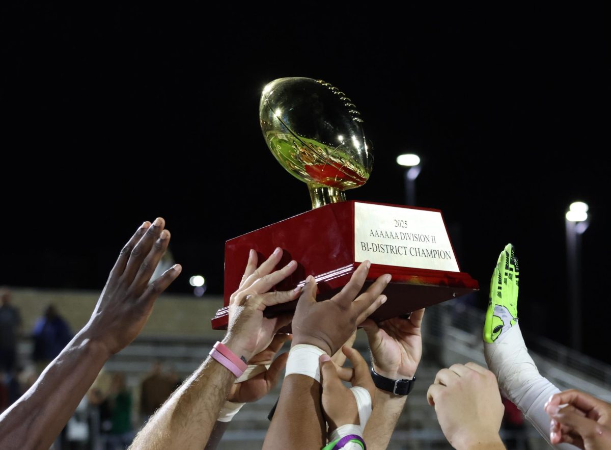 ALL HANDS IN. After winning the Bi-District championship game, players lift and praise their trophy in celebration. The Wildkat football team has won Bi-District champs for three years in a row.