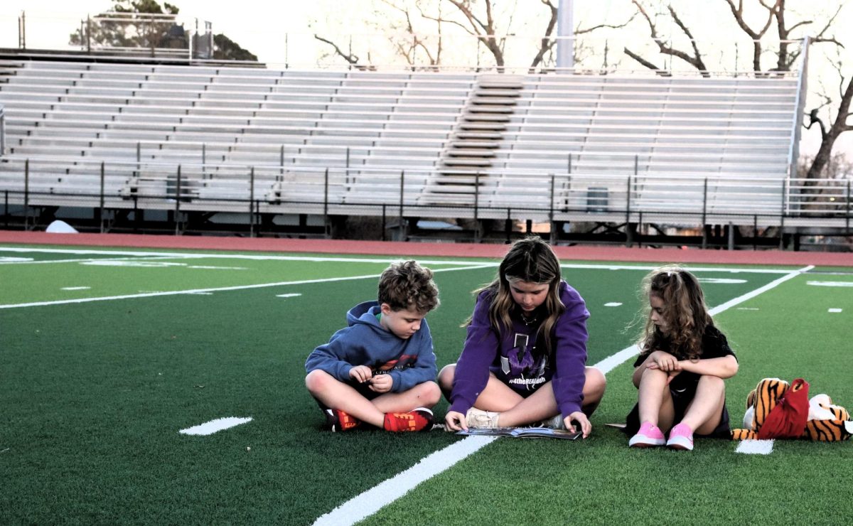 UNDER THE LIGHTS.  On Read Across America Day, freshman Caroline Williams reads to Beckett Blakelock and Maddie Arthur. The event paired high school students  with younger students to celebrate Dr. Seuss's birthday. The event included free books, Kona Ice and face painting by student volunteers.